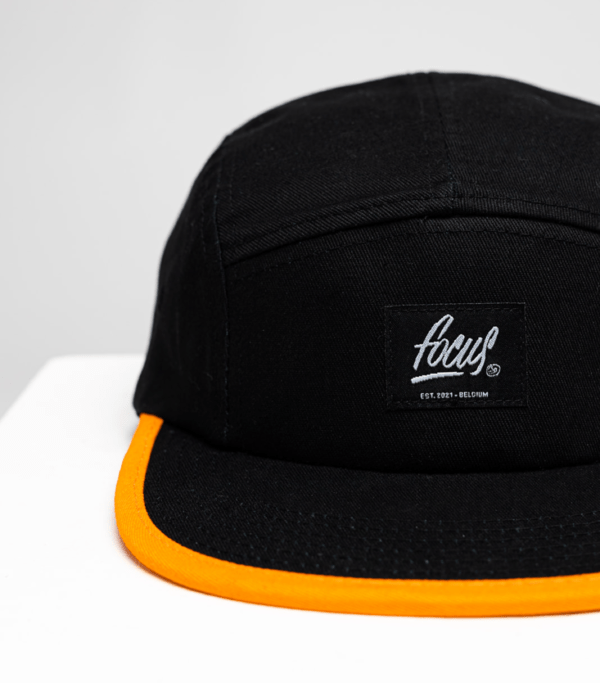 black 5 panel cap with orange lip and woven focus label on the front panel