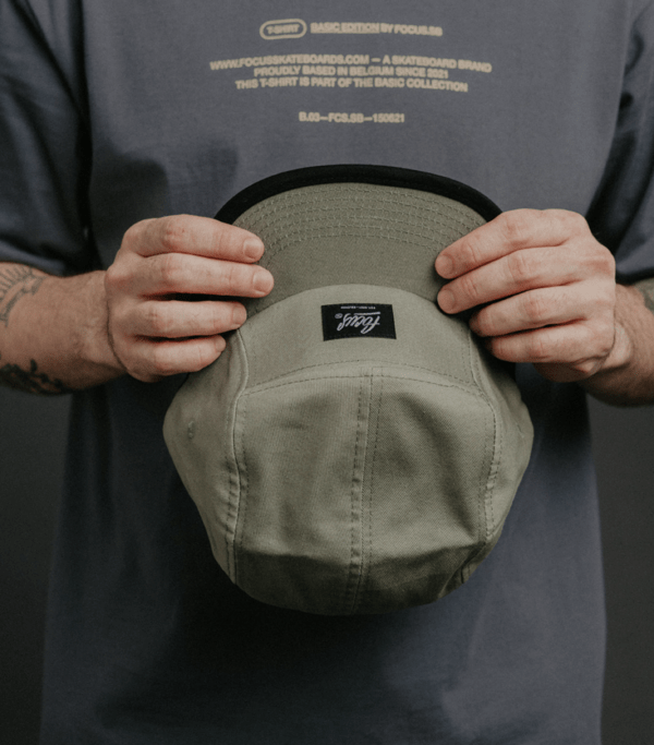 hands holding the green 5 panel cap with grey t-shirt