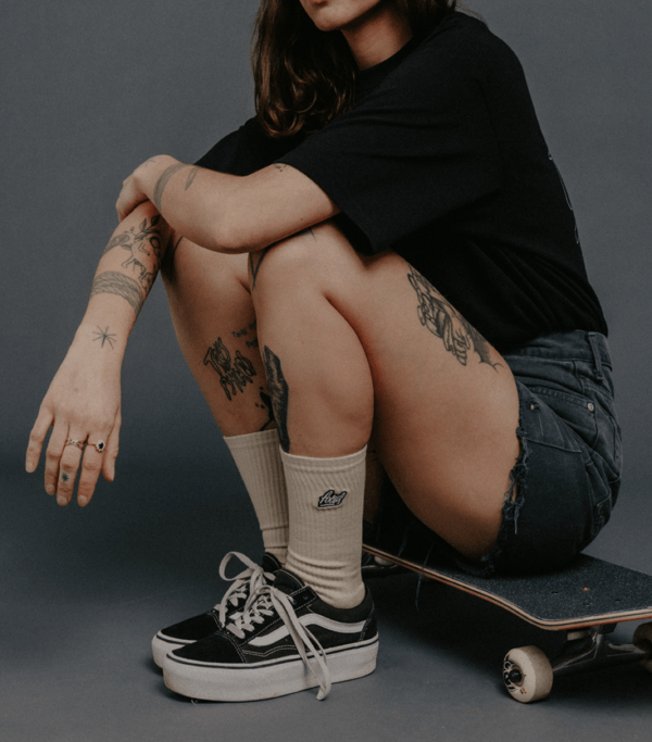 female model sitting on skateboard wearing focus brown socks and black t-shirt